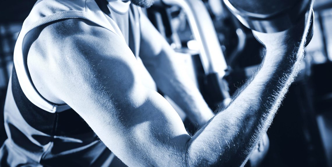 Arm of strong man doing exercise with barbell