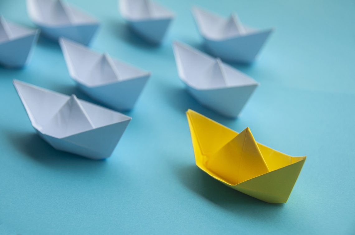 Leadership Concept - Yellow color paper ship origami leading the rest of the white paper ship on blue cover background. Copy space